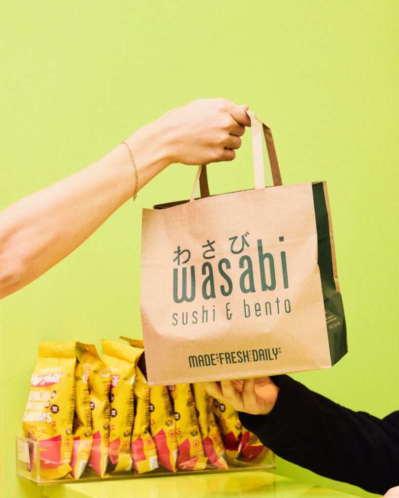 A person hands a brown paper bag labeled 