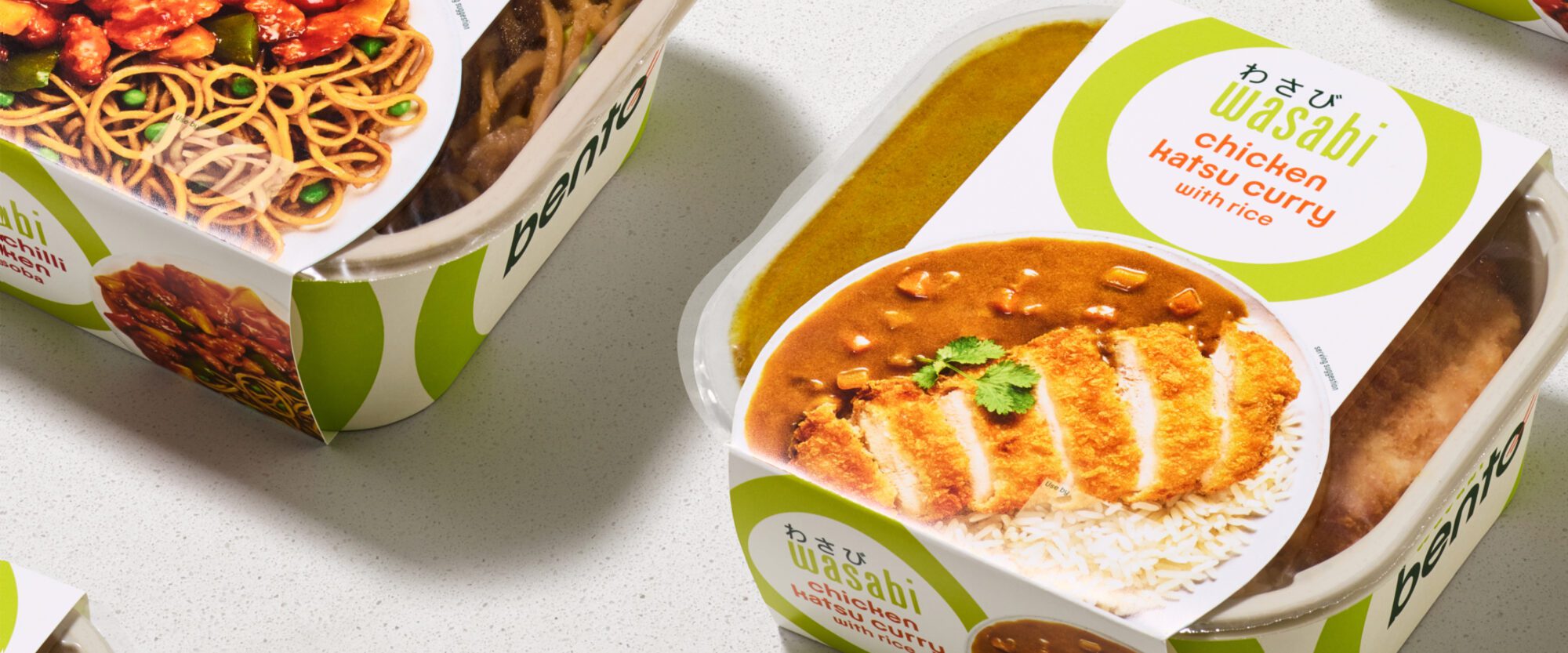 Close-up of packaged Wasabi brand meals, featuring Chicken Katsu Curry with rice. The packaging includes vibrant images of the dish, showing breaded chicken slices with curry sauce, served with rice. Other boxed meals are partially visible.