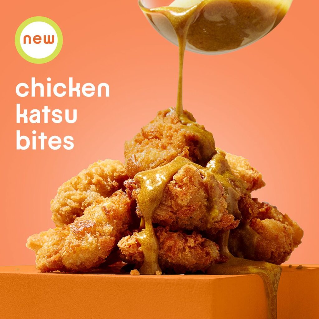 A stack of crispy chicken katsu bites on an orange surface is being drizzled with a golden sauce from a spoon. The text reads 